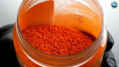 Close-up image of a gloved hand scooping undissolved FD & C Yellow 5 dye from a glass jar.