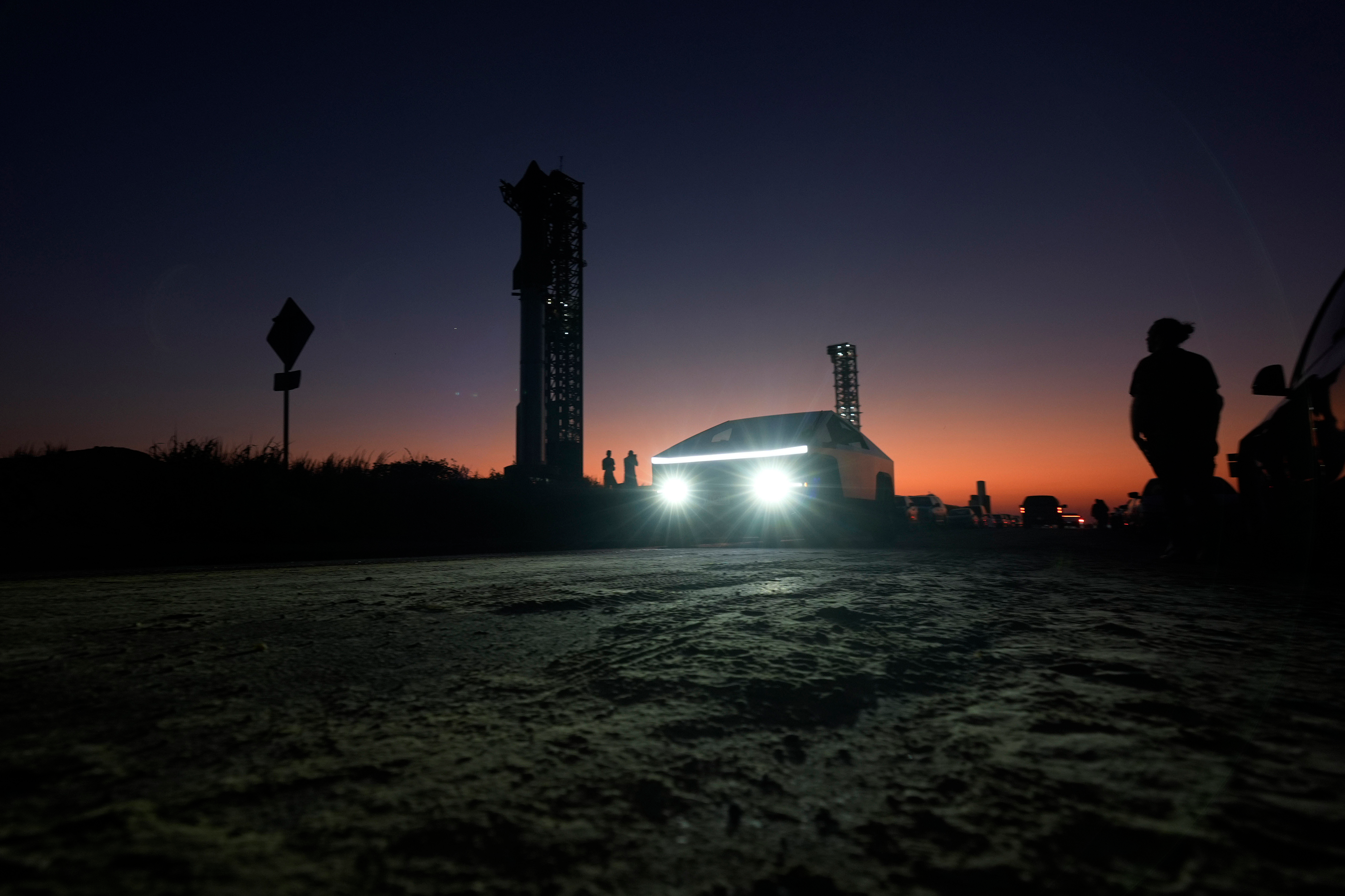 A Tesla Cybertruck passes as the sun sets behind SpaceX's mega rocket Starship, on Oct. 12, 2024, in Boca Chica, Texas.