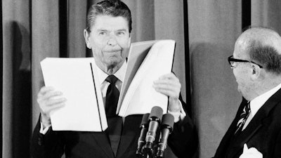 President Ronald Reagan displays reports given to him by J. Peter Grace, right, of the Private Sector Survey on Waste and Cost Control in Government, at the White House in Washington, Jan 16, 1984.