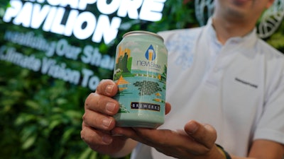 Nick Chow, part of the COP29 Singapore Pavilion team, poses for a photo with NEWBrew, beer made with treated wastewater, during the COP29 U.N. Climate Summit, Friday, Nov. 15, 2024, in Baku, Azerbaijan.