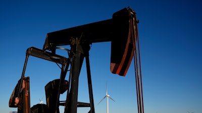 A pumpjack operates in the foreground as wind turbines at the Buckeye Wind Energy wind farm rise in the distance, Monday, Sept. 30, 2024, near Hays, Kan.