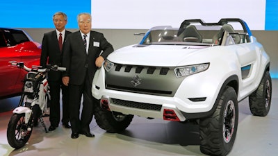 Suzuki Motor Corp. President and Chairman Osama Suzuki, right, and Vice President Osamu Honda pose with a Suzuki X-Lander hybrid concept car on display at a media preview for the Tokyo Motor Show in Tokyo, Nov. 20, 2013.