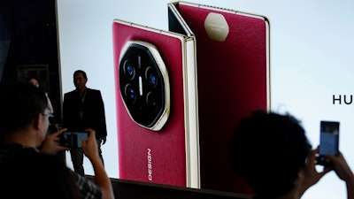 Visitors take pictures in-front of a giant billboard display of Huawei's industry's first tri-foldable phone during the opening of its global sales in Kuala Lumpur, Malaysia, Tuesday, Feb. 18, 2025.
