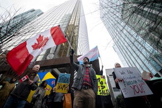 People wave flags and hold signs during a protest outside of the U.S embassy in Vancouver, British Columbia, Tuesday, March 4, 2025.