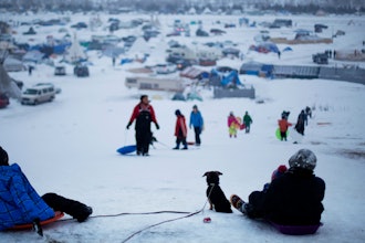 In this Thursday Dec. 1, 2016 file photo, the Oceti Sakowin camp where people have gathered to protest the Dakota Access oil pipeline stands in the background as a children sled down a hill in Cannon Ball, N.D.