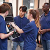 An engineer shows apprentices how to use a CNC machine.