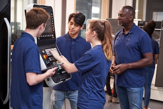An engineer shows apprentices how to use a CNC machine.