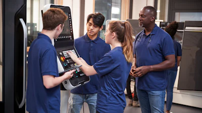 An engineer shows apprentices how to use a CNC machine.