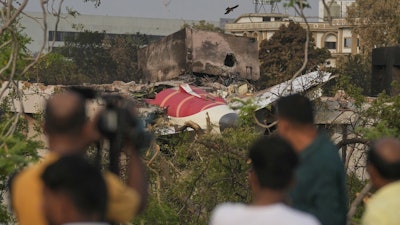 Onlookers watch wreckage from Thursday's Air India plane crash lying atop a building in Ahmedabad, India, Saturday, June 14, 2025.