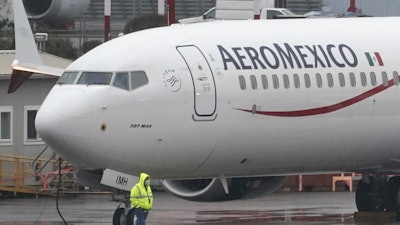A worker wearing a mask walks past a Boeing 737 Max 9 as it is prepared for a flight from Renton Municipal Airport, Nov. 18, 2020, in Renton, Wash.