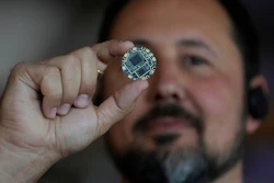 Circular electronic microchip held between fingers, showcasing intricate circuit board design