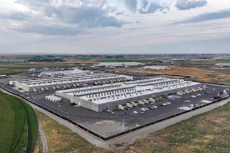 Aerial view of large white warehouse complex with parking lot in rural landscape