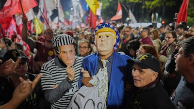 Protesters wearing masks of U.S. President Donald Trump and former President Jair Bolsonaro as a prisoner, protest Trump's announcement of 50% tariffs on Brazilian goods, in Sao Paulo, Thursday, July 10, 2025.