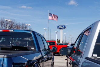 Ford dealership with blue and red trucks under clear sky with American flag