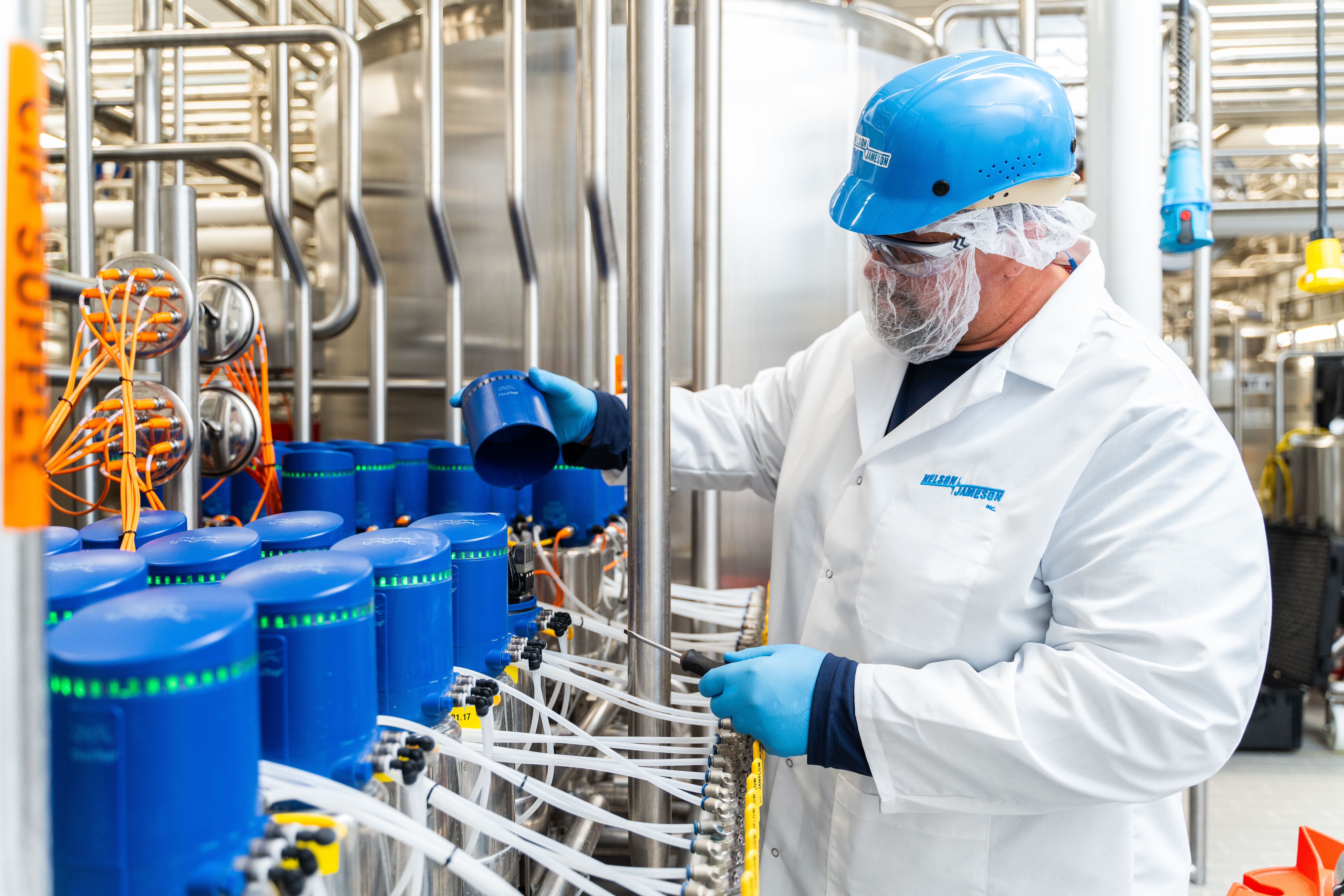 Worker in blue helmet and white lab coat operating industrial bottling machinery