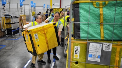 Amazon employees load packages on carts at Amazon's DAX7 delivery station, July 16, 2024, South Gate, Calif.