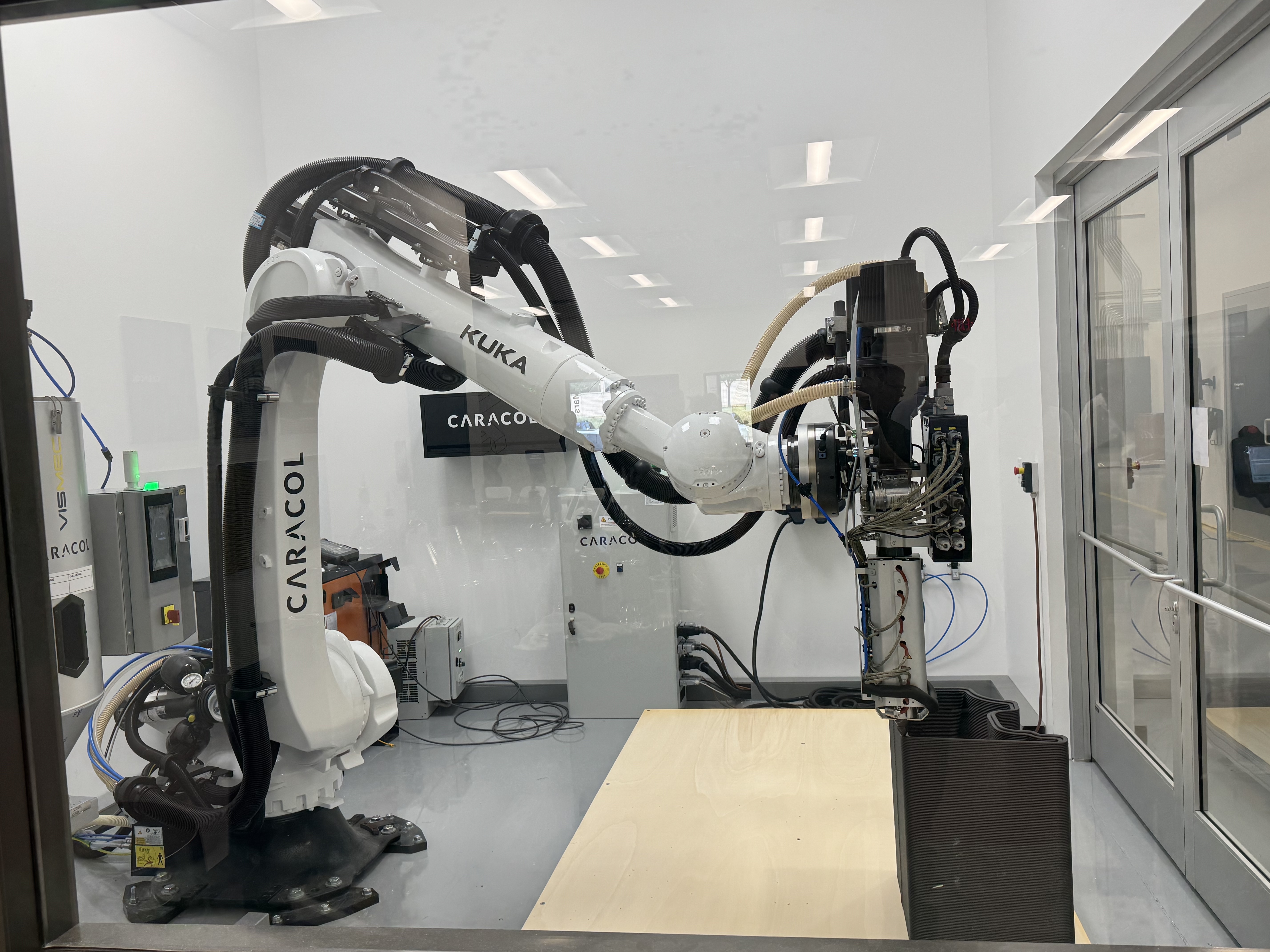 White Kuka industrial robotic arm 3D printing at Caracol's facility.