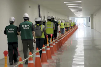 Construction workers in safety gear walking through hallway lined with orange traffic cones