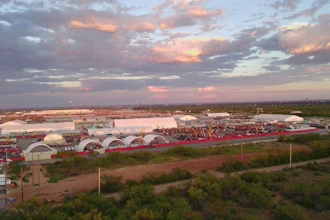 Sunset over industrial complex with white arched buildings and red perimeter fencing