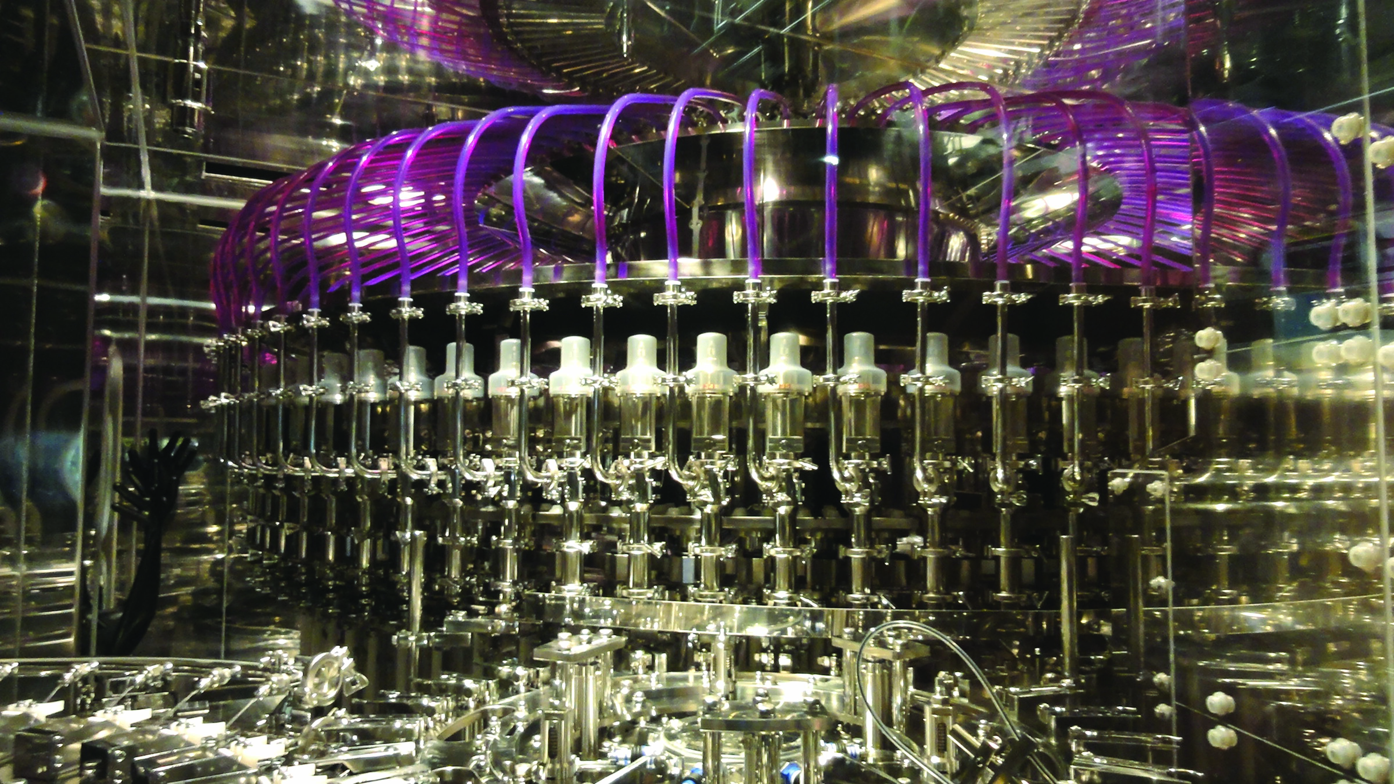 Industrial bottling machine with metallic components and purple tubing