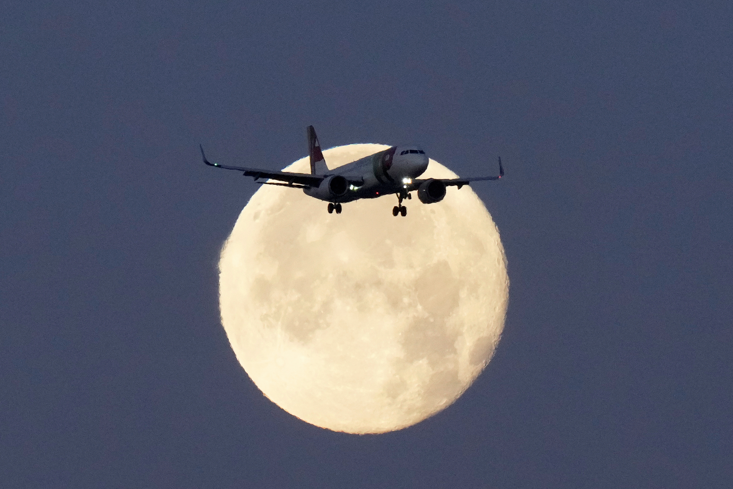 A TAP Air Portugal Airbus A320 is silhouetted against the setting moon while approaching for landing in Lisbon, Portugal, June 23, 2024.