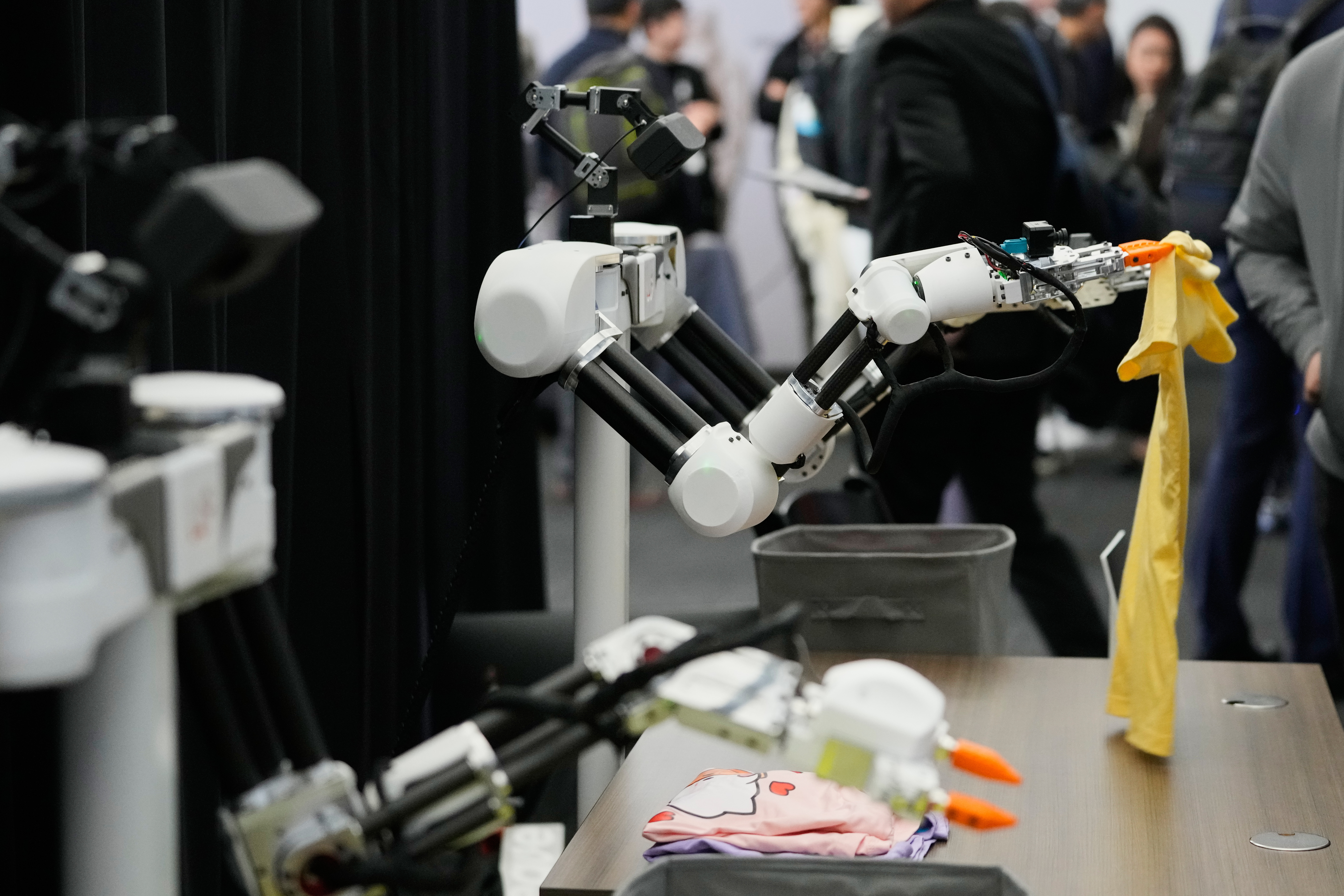 Robots, made by Weave Robotics, fold clothes inside the exhibition room at the Humanoids Summit, Thursday, Dec. 11, 2025, in Mountain View, Calif.