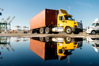 Yellow semi-truck with shipping container reflected in water at industrial port