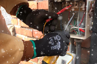 Technician wearing protective gloves repairing electrical panel near brick wall