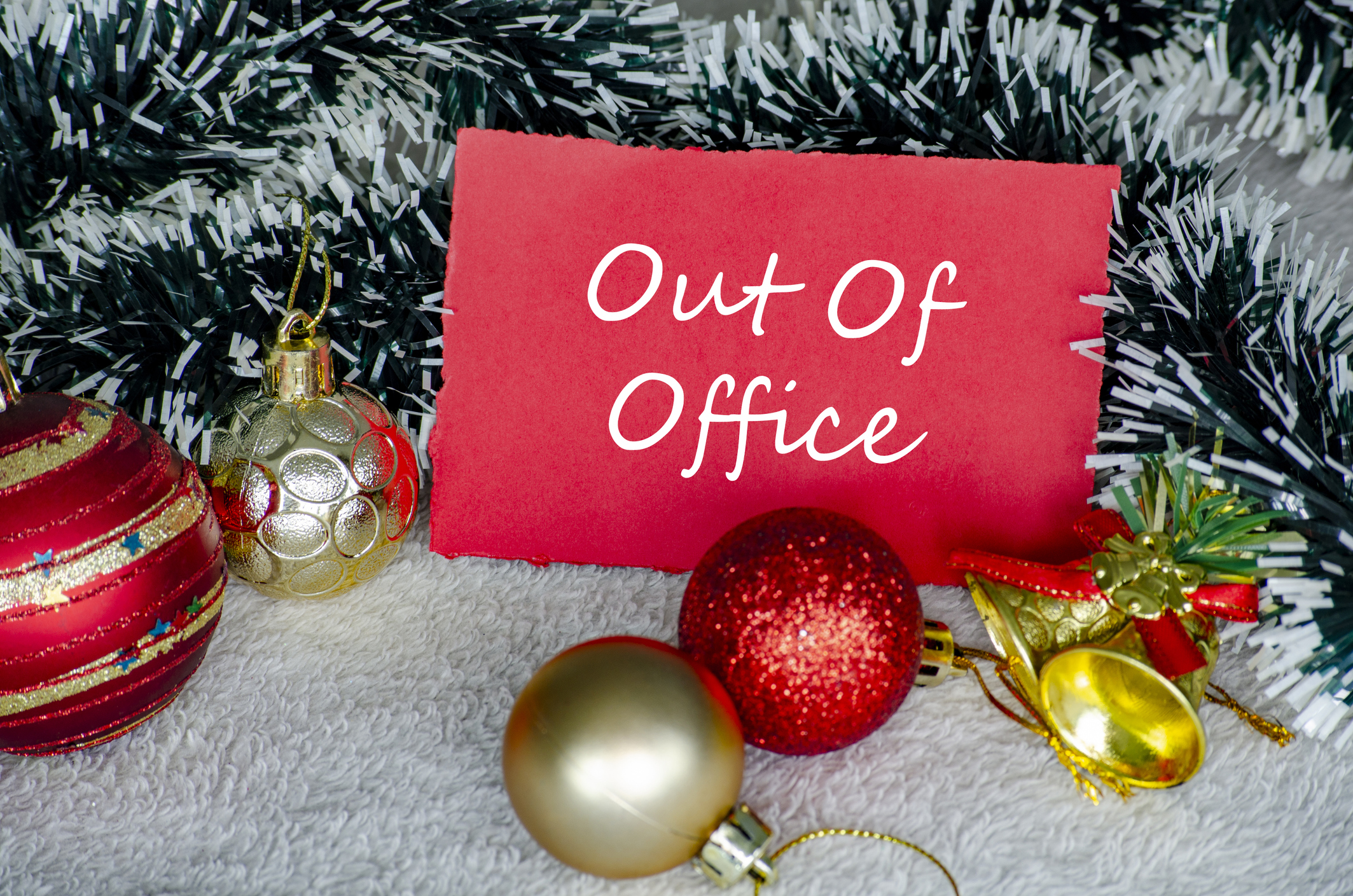 AI generated caption: Holiday scene with 'Out of Office' sign and festive ornaments on tinsel background.