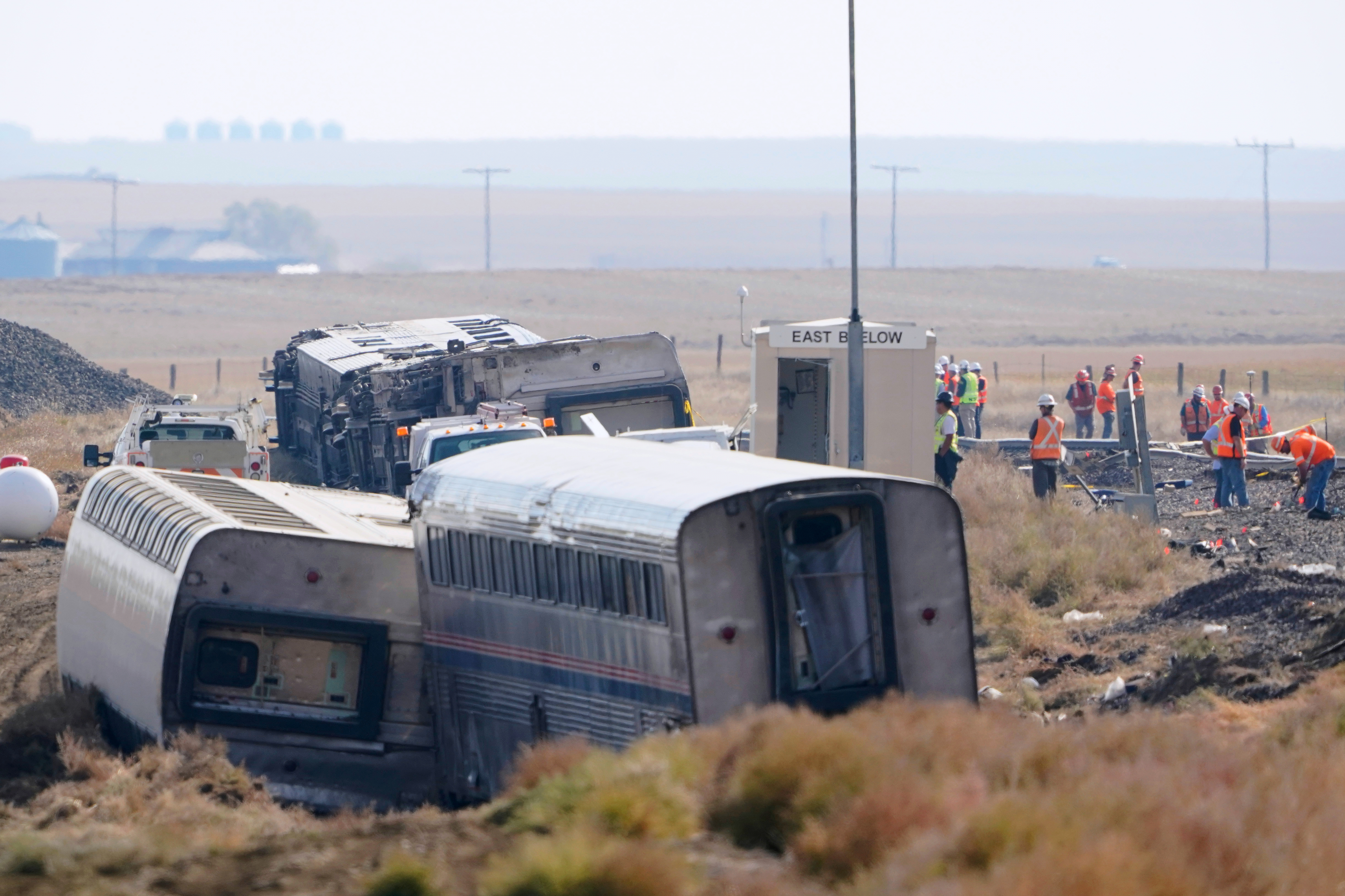 In this Sept. 27, 2021, file photo, workers stand near train tracks next to overturned cars from an Amtrak train that derailed near Joplin, Mont.