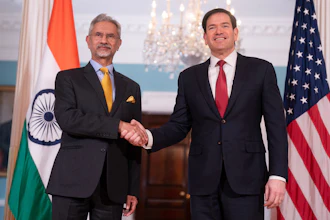 Indian and US diplomats shaking hands in formal diplomatic setting with national flags