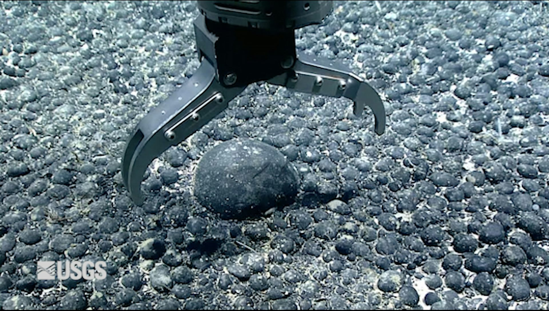 A metal claw reaches for an iron and manganese nodule on the seabed for testing.