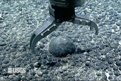A metal claw reaches for an iron and manganese nodule on the seabed for testing.