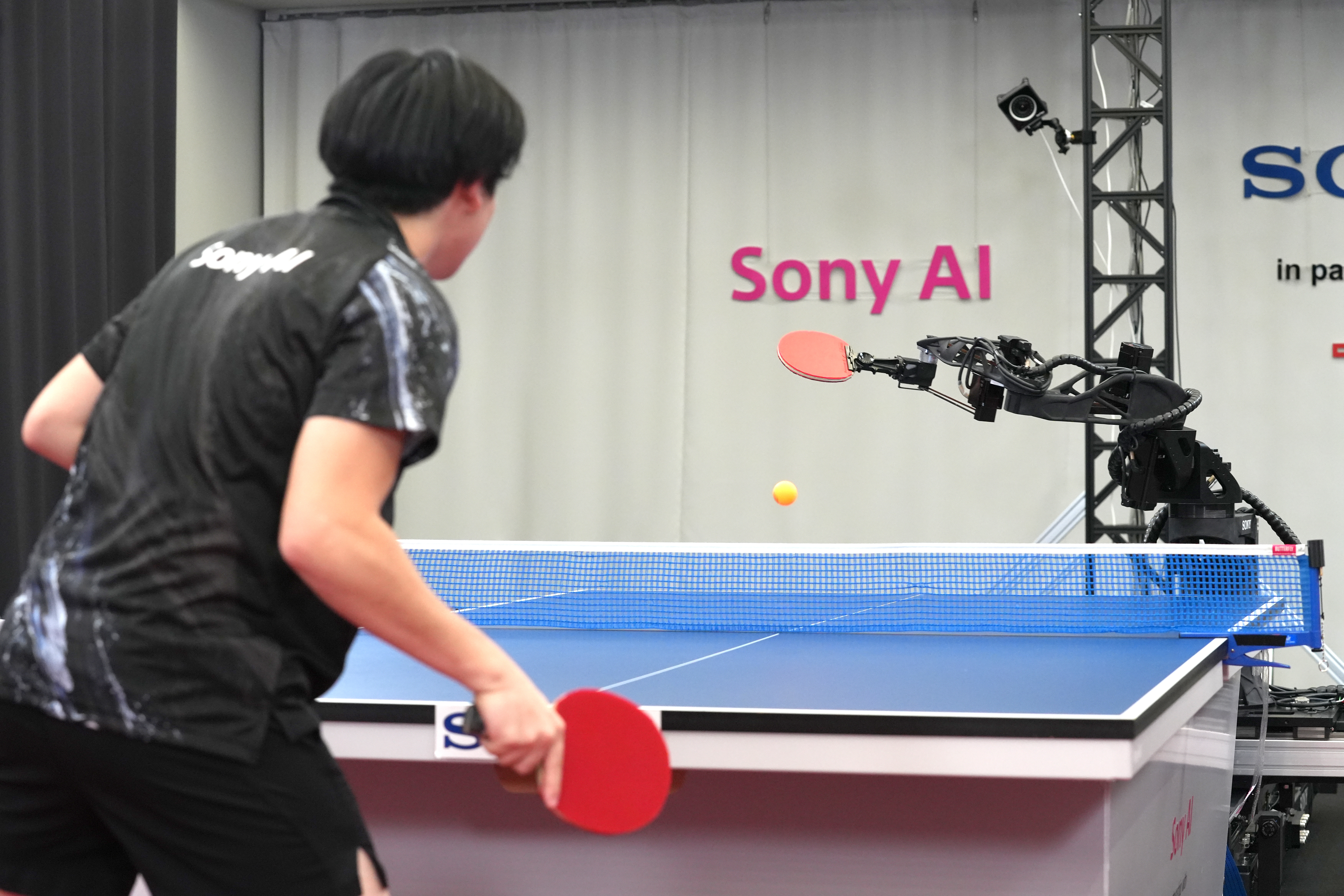 A table tennis robot built by Sony maneuvers to hit the ball back to its human opponent, Akito Saeki, during a match in Tokyo, Dec. 2025.