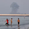 Three boys play in the shallow waters of the Strait of Hormuz as a plume of smoke rises from an explosion in the background off Bandar Abbas, Iran, July 13, 2026.