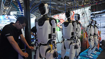 A worker reacts near a line of humanoid robots displayed at the World AI Conference in Shanghai, Friday, July 17, 2026.
