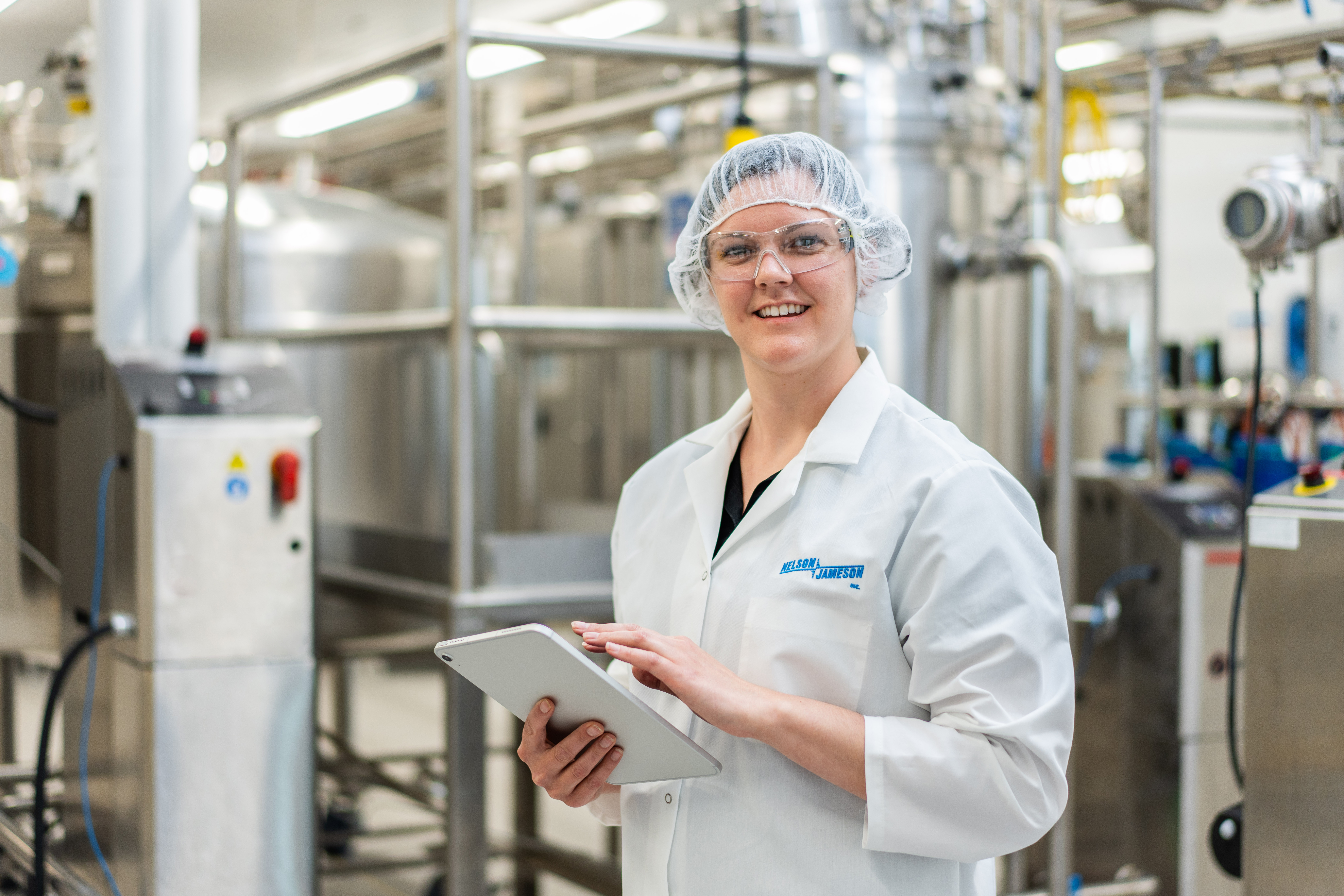 Female technician in white lab coat holding tablet in modern manufacturing facility