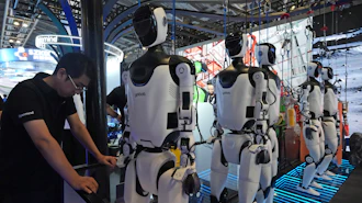 A worker reacts near a line of humanoid robots displayed at the World AI Conference in Shanghai, Friday, July 17, 2026.