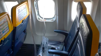 This undated photo provided by the National Transportation Safety Board on Thursday, Aug. 13, 2026, shows the shattered window on a Ryanair plane that was broken by a stray engine part shortly after takeoff, causing a man's head to be sucked into the hole.