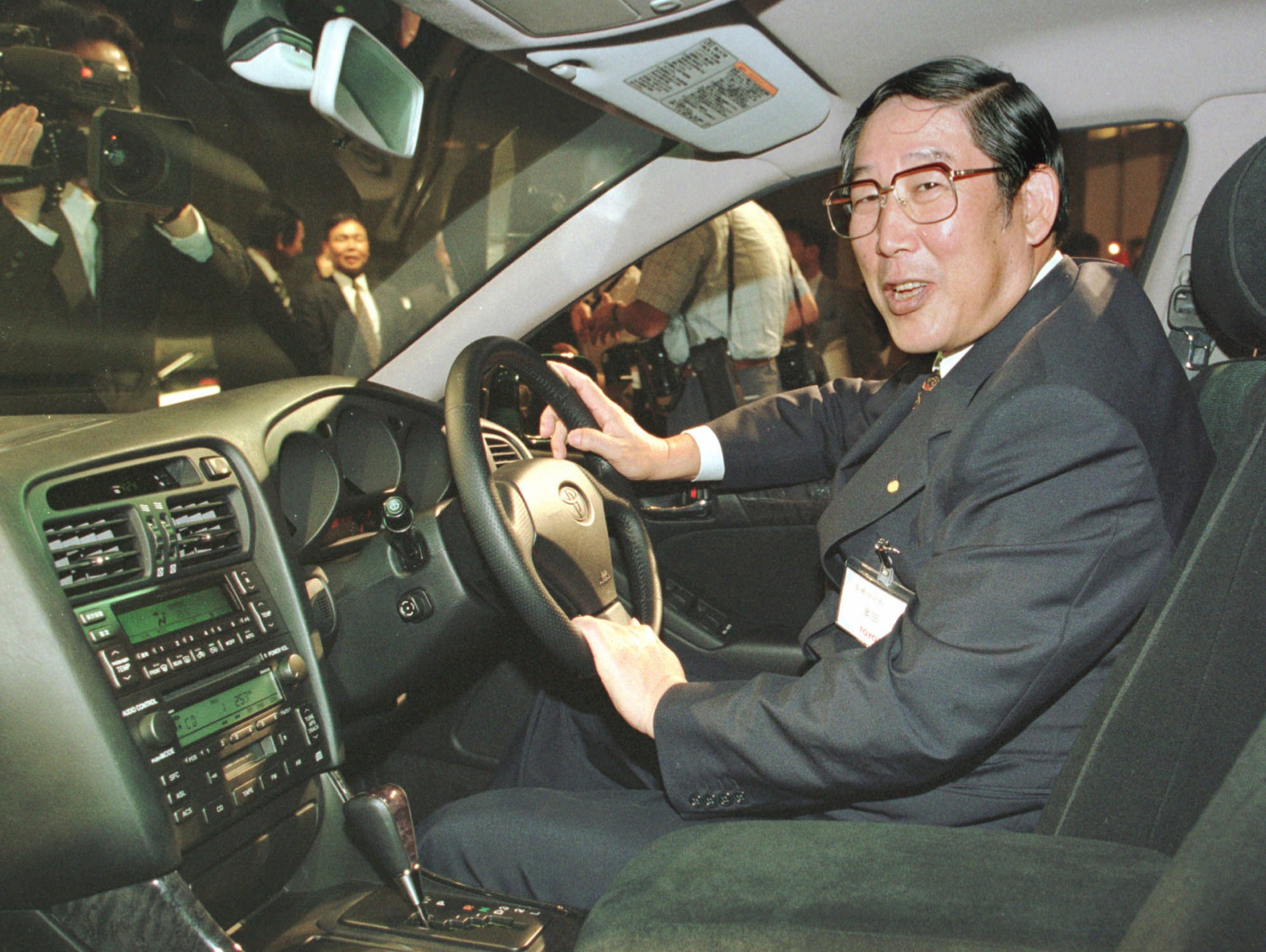 Hiroshi Okuda, then, president of Toyota Motor Corp., smiles as he sits at the steering wheel of the 'Aristo,' Toyota's remodeled sports sedan during a press conference at a Tokyo hotel, Aug. 27, 1997.