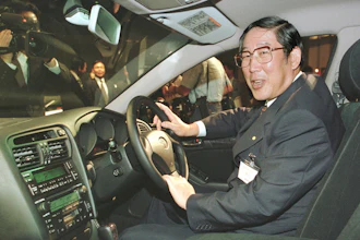 Hiroshi Okuda, then, president of Toyota Motor Corp., smiles as he sits at the steering wheel of the 'Aristo,' Toyota's remodeled sports sedan during a press conference at a Tokyo hotel, Aug. 27, 1997.