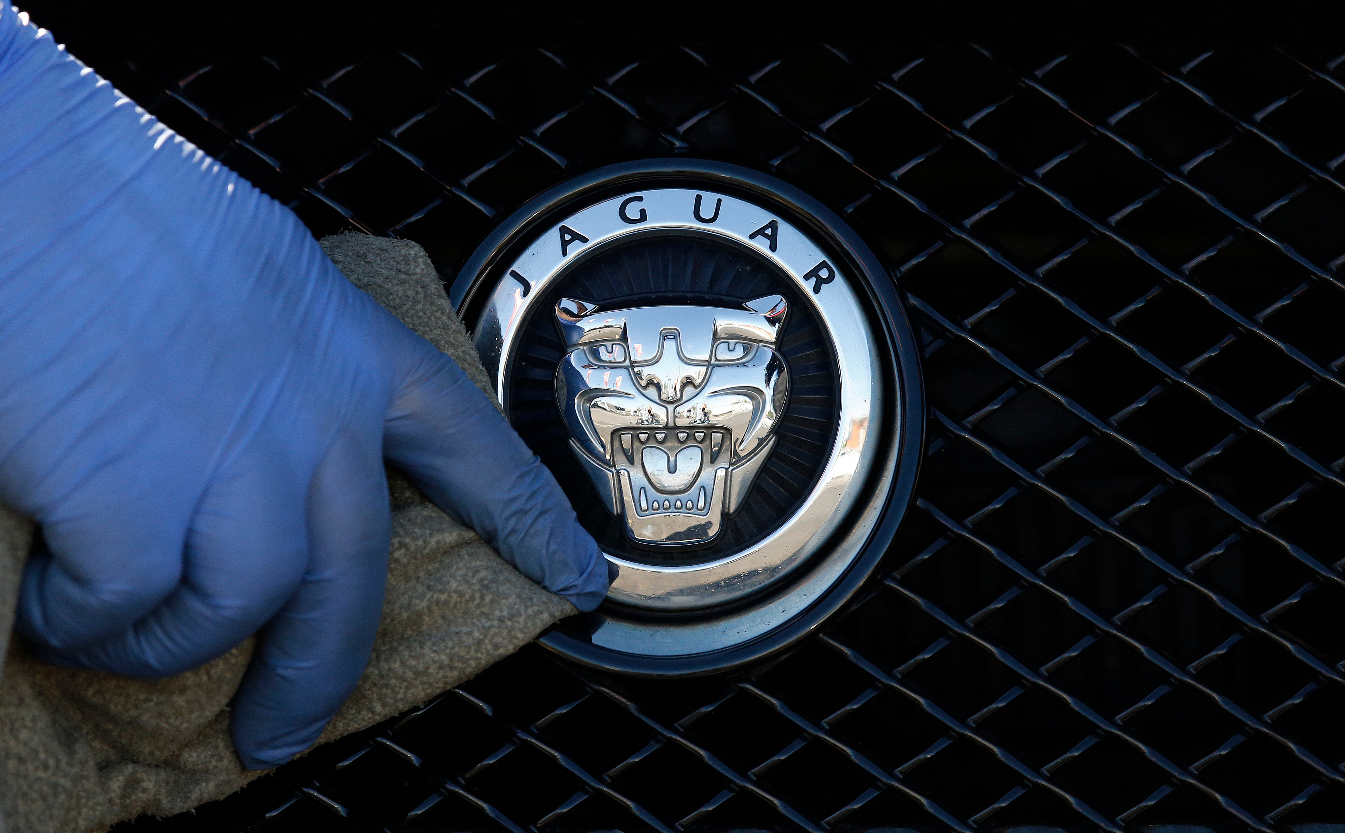 A worker polishes a Jaguar logo on a car at a Jaguar dealer in London, Wednesday Sept. 28, 2016.