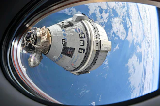 Boeing Starliner spacecraft docked to International Space Station above Earth with blue sky and clouds visible