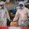 Two industrial workers in white protective suits and respirators at a manufacturing facility with Manufacturing Now logo