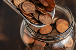 Copper pennies pouring into a glass jar for savings and financial planning