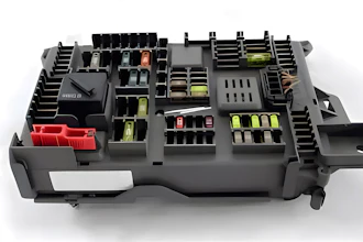 Automotive fuse box with organized yellow and red fuses, relays, and electrical components in black housing