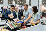 Professionals examining tools and equipment at a trade show booth with green lanyards