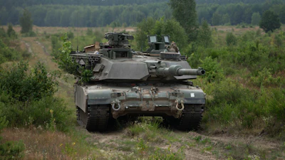 Military tank positioned in forested terrain with coniferous trees and cleared ground in background