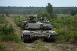 Military tank positioned in forested terrain with coniferous trees and cleared ground in background