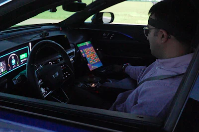Person playing retro video game on dashboard screen inside convertible car